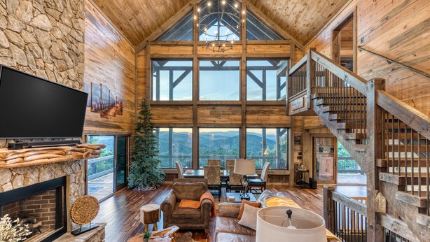 En rummelig stue med en pejs af natursten, træloft og store vinduer med udsigt til bjergene.