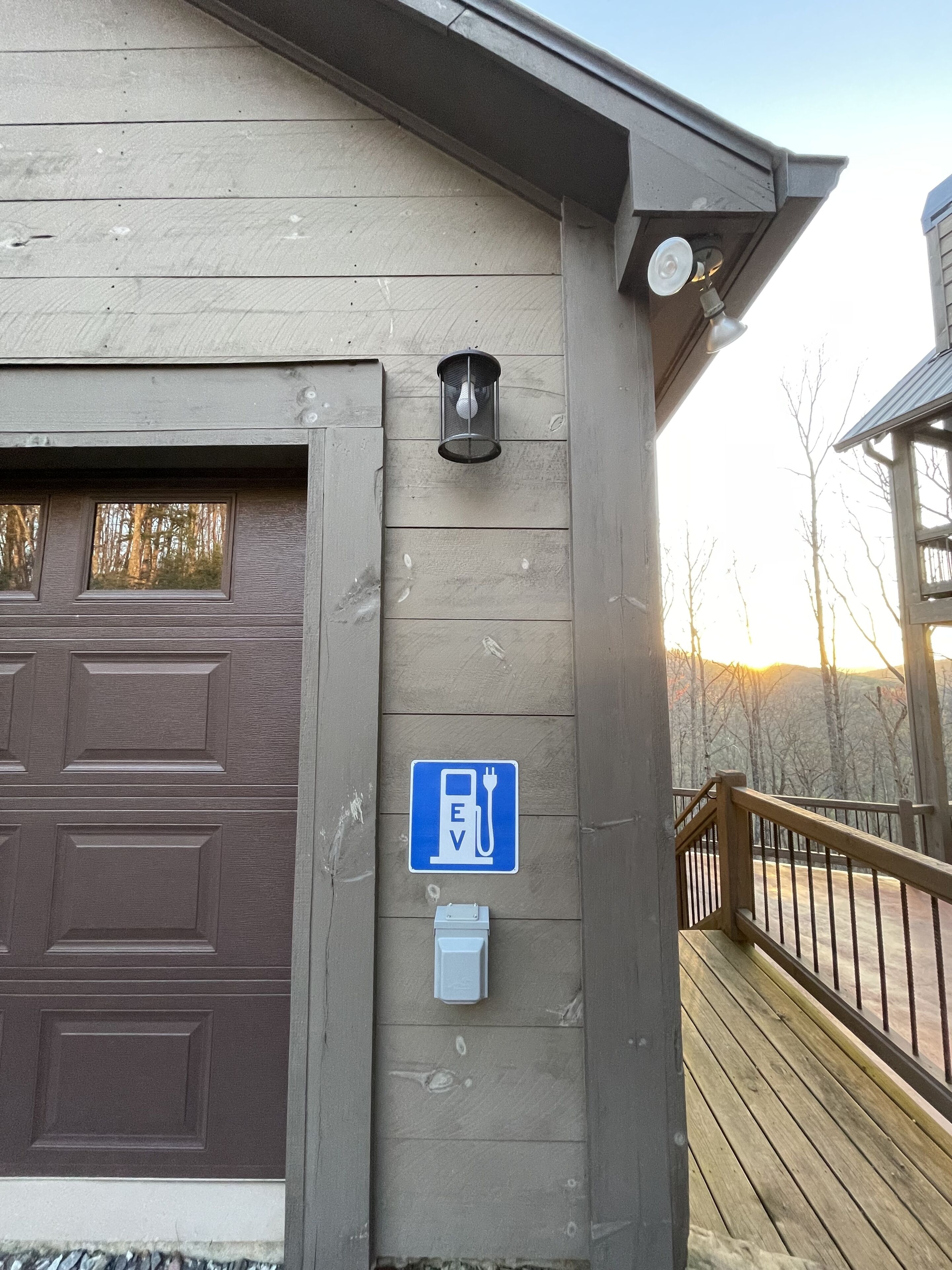 A building with a brown garage door, a blue EV charging station sign, and a small white box on the wall.