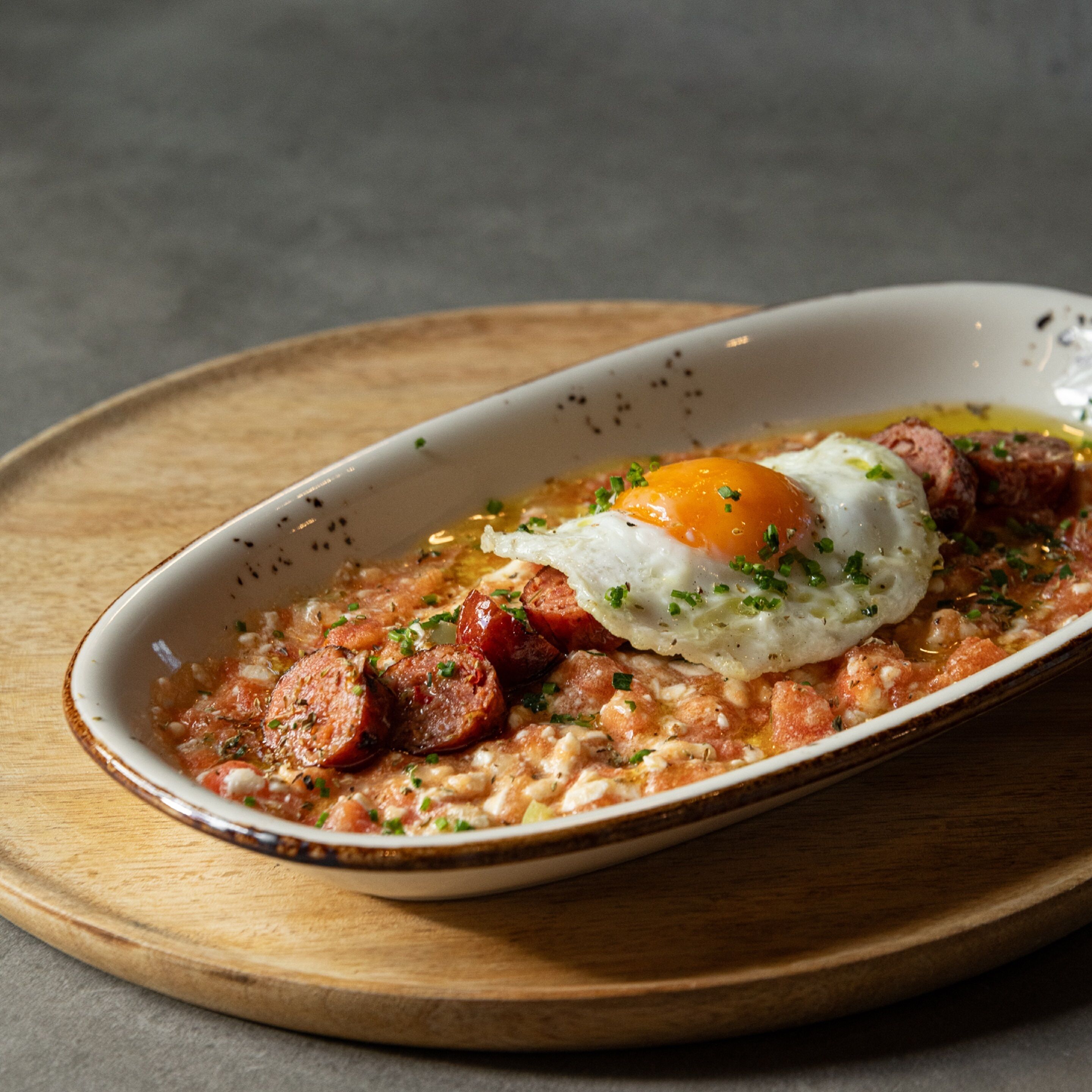 A dish with sausage, egg, and herbs on a wooden board.