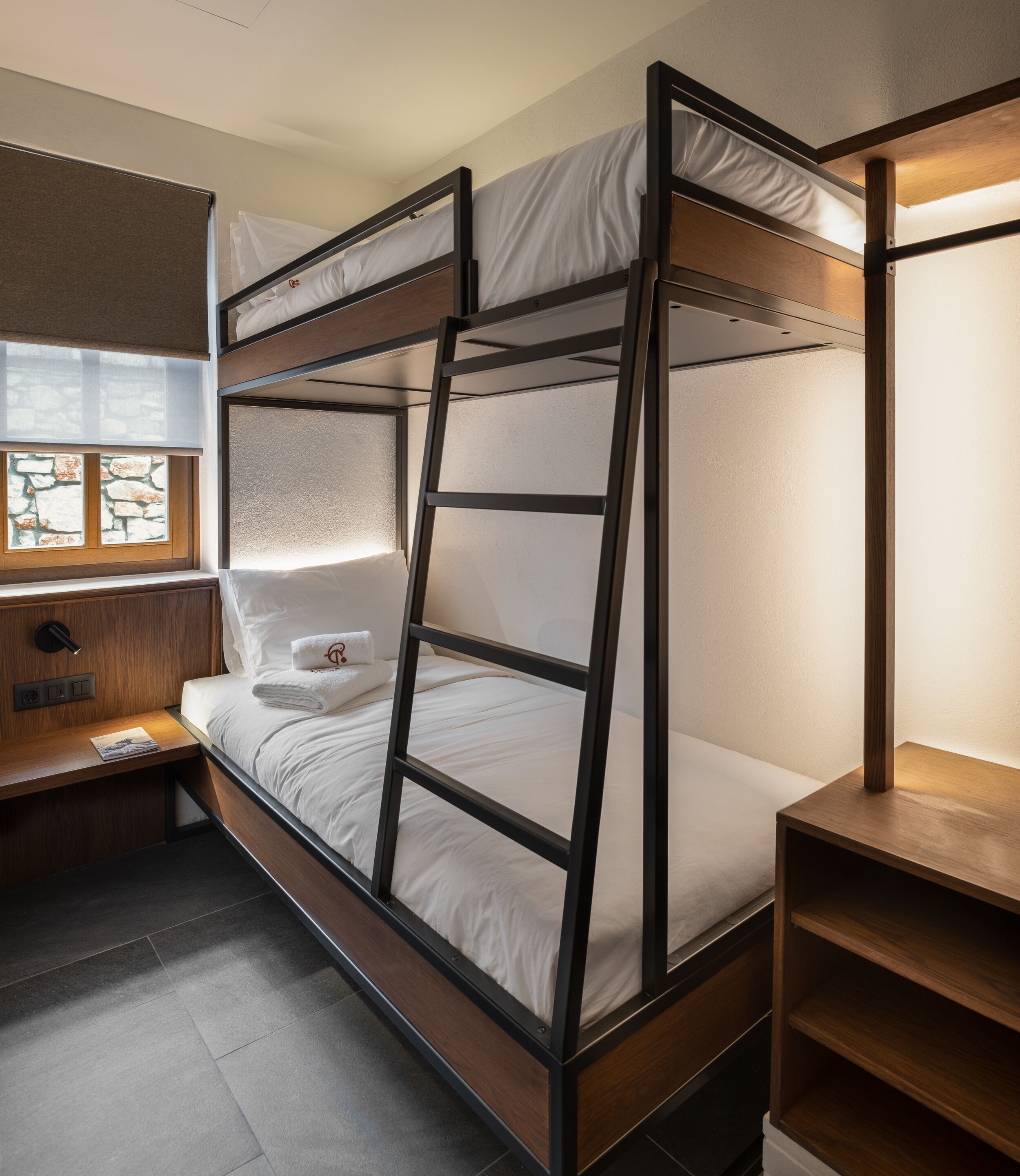 Ein Stockbett mit einer Leiter, ein Nachttisch mit einer Lampe und ein Fenster mit Steinwänden.
