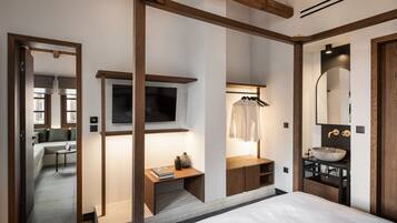 Ein modernes Schlafzimmer mit einem großen Bett, einem an der Wand befestigten Fernseher, einem Holztisch und einem Badezimmer mit einem großen Spiegel und Waschbecken.