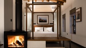 Um interior moderno com lareira central, vigas de madeira, uma cama e obras de arte emolduradas nas paredes.