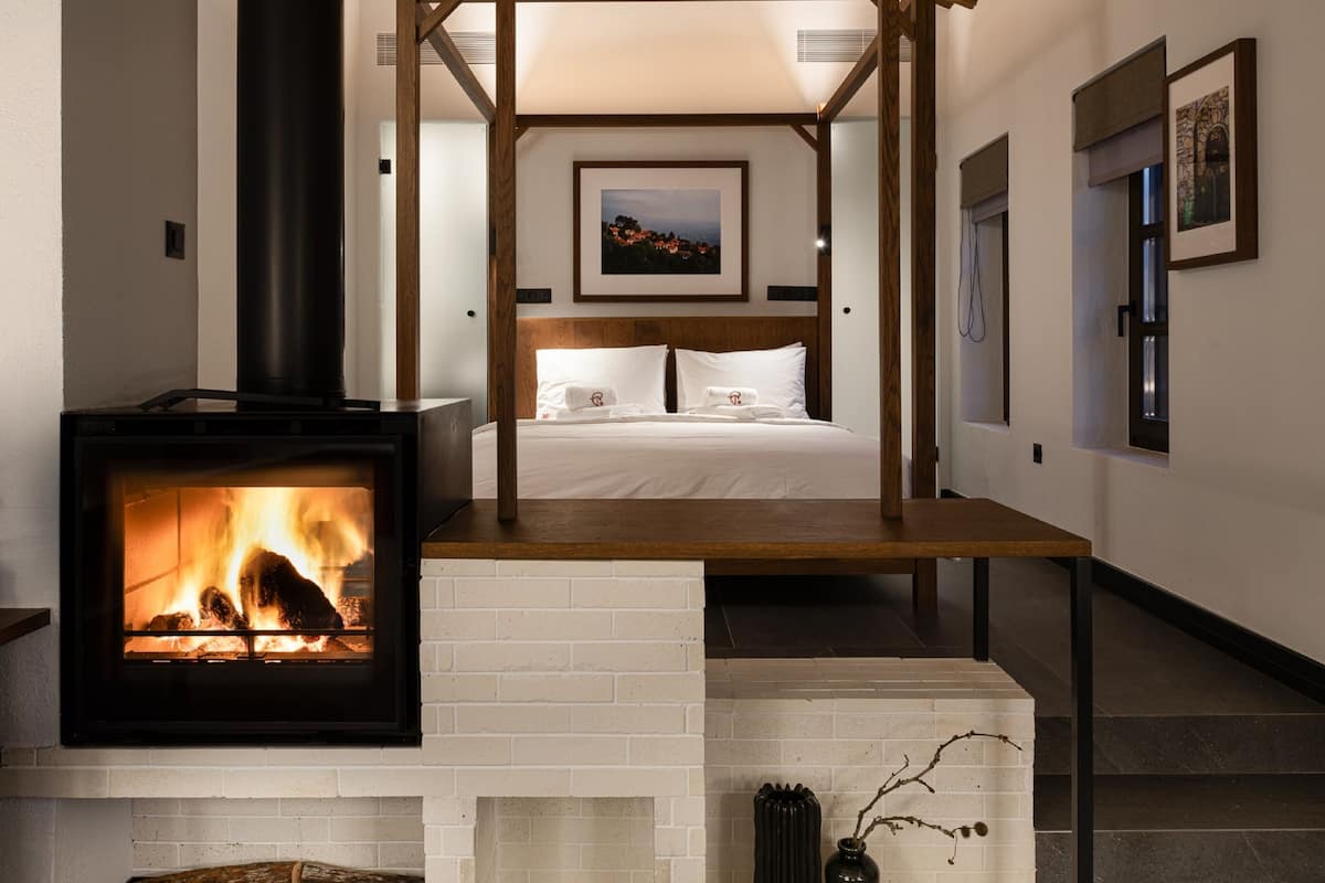 Un interior moderno con una chimenea central, vigas de madera, una cama y obras de arte enmarcadas en las paredes.