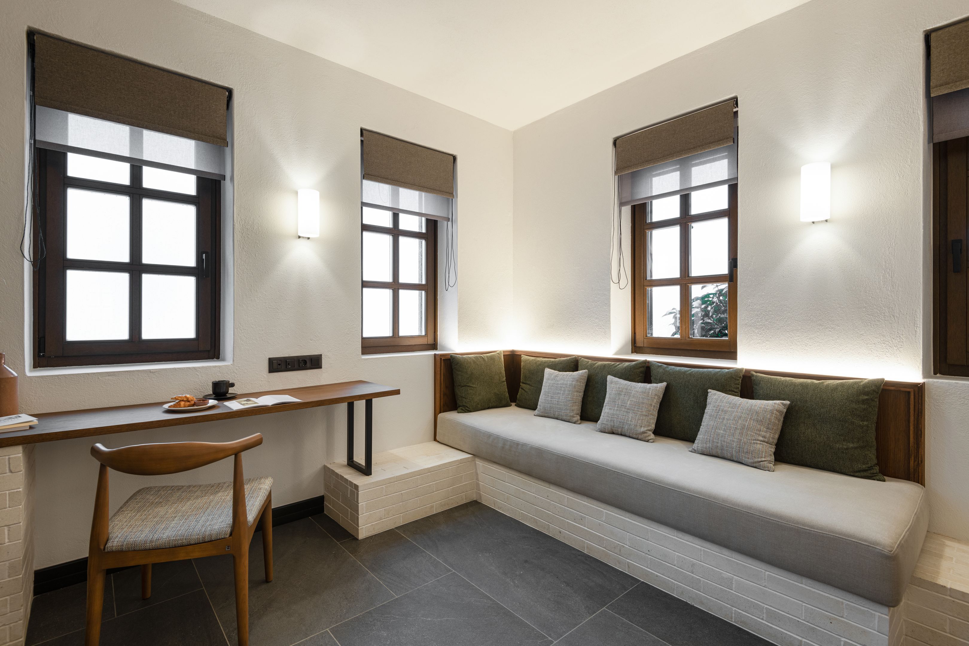 A modern room with a built-in bench, a desk, and two windows with blinds.