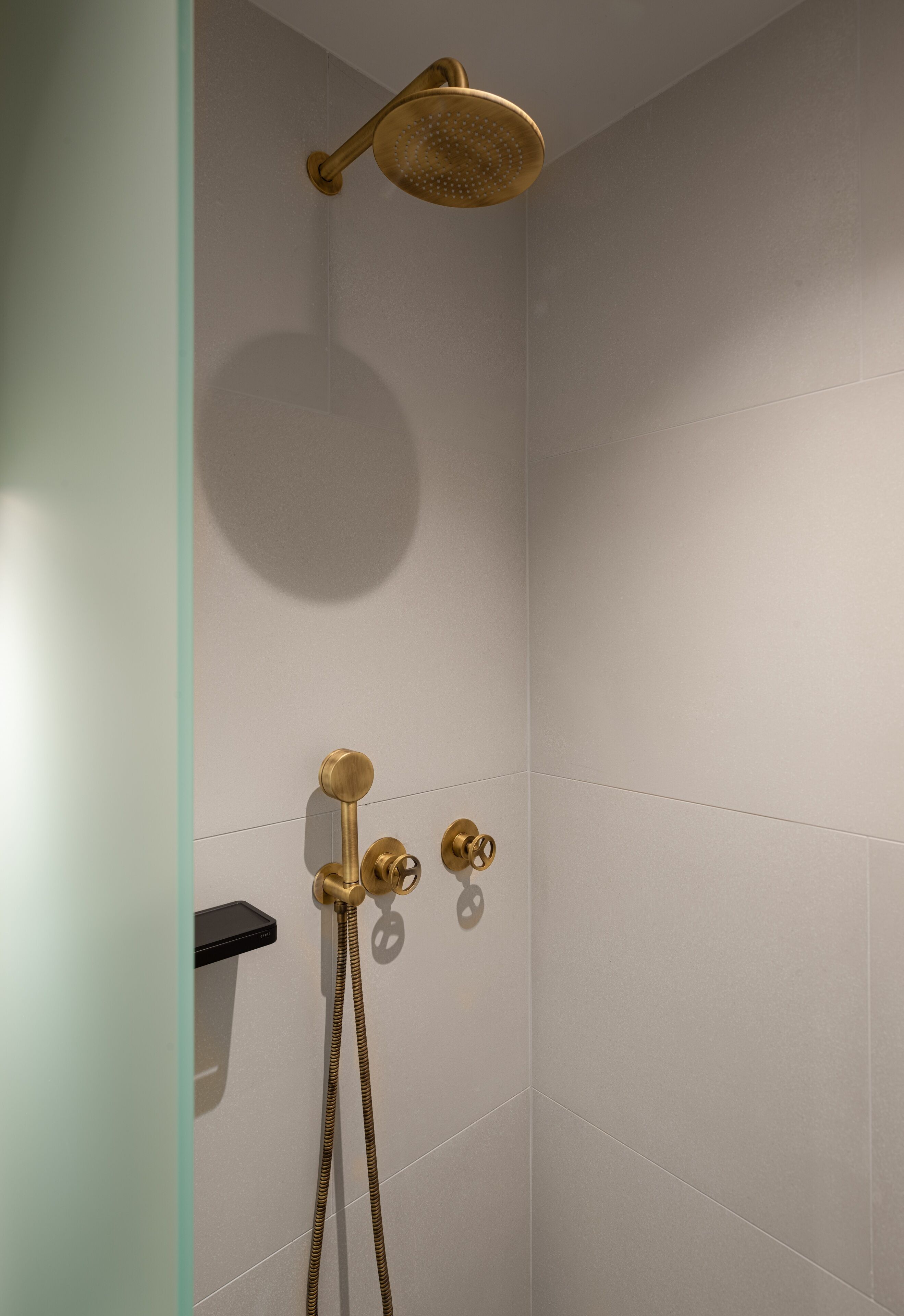Ducha con cabezal dorado y mandos, un rociador de mano y un panel de control en la pared.