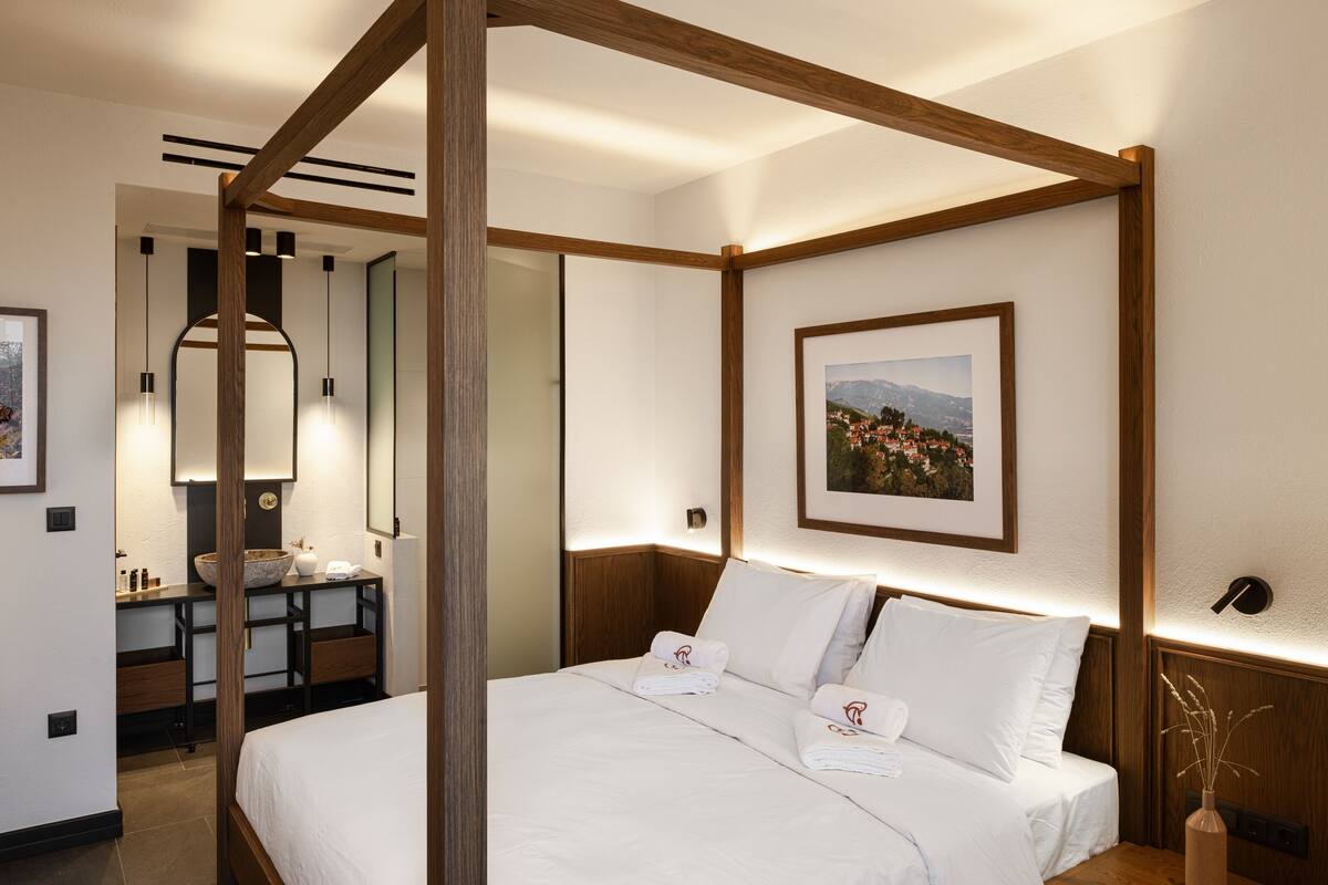 Una cama con dosel, ropa de cama blanca, cabecera de madera y una mesita de noche con un florero.
