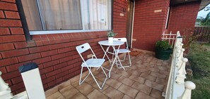 An outdoor patio with a brick wall, a white metal table and chairs, and a potted plant.