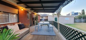 A covered outdoor patio with a wooden deck, a table and chairs, a sofa, and a potted plant.