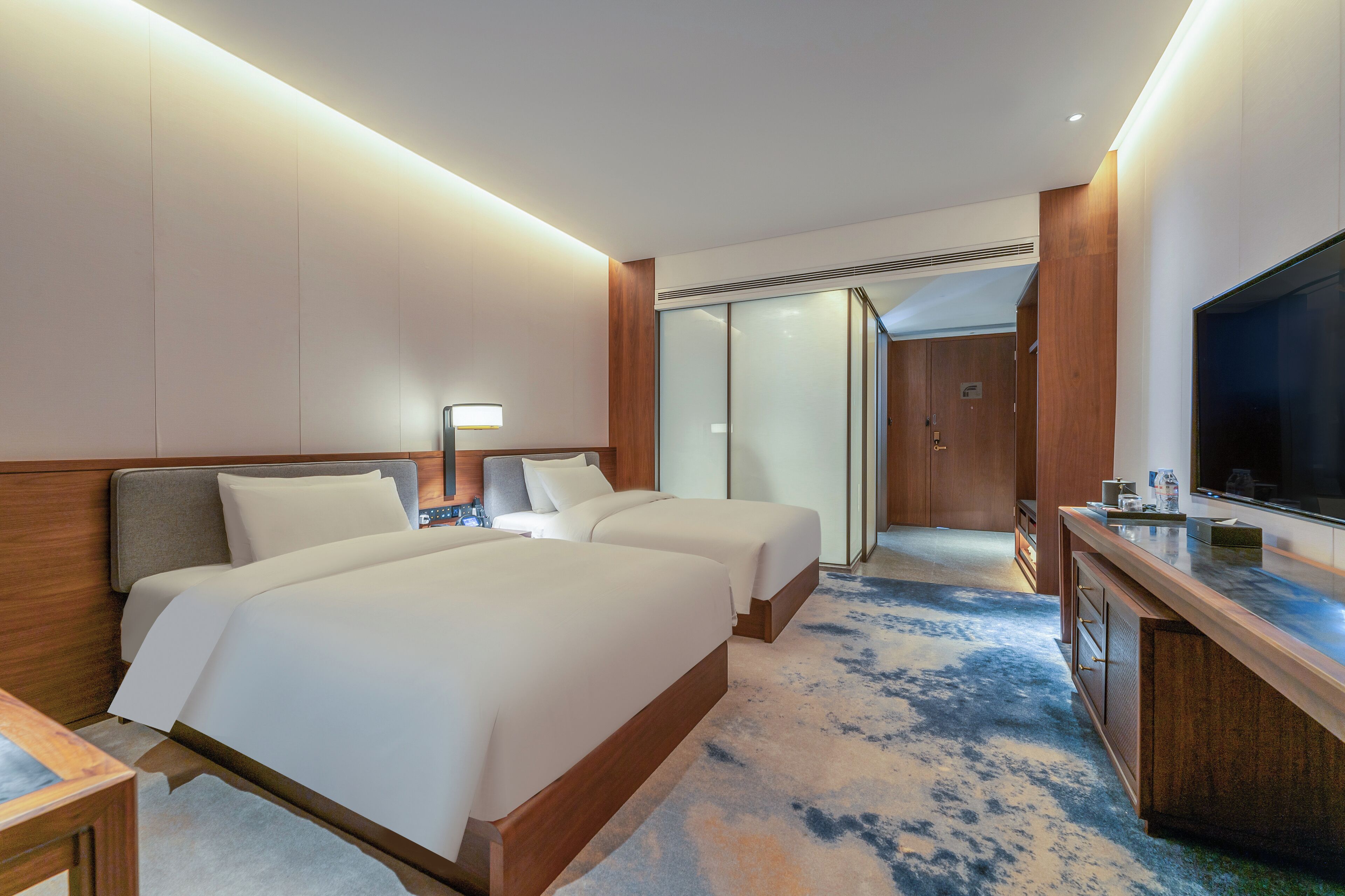 Une chambre d’hôtel avec deux lits, une télévision, un bureau et une salle de bain visible à travers une porte en verre.
