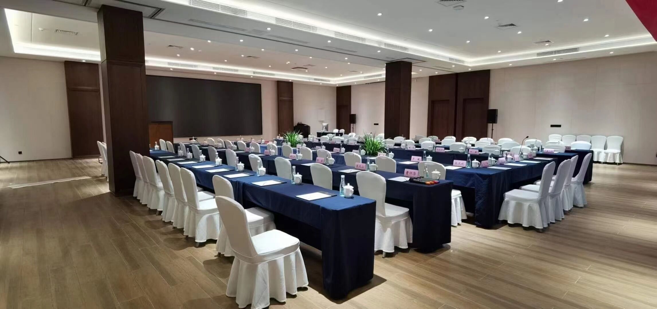 A conference room with multiple tables, white chairs, and a large screen.