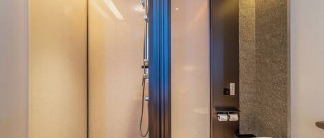 A modern bathroom with a glass-enclosed shower, a toilet, and a towel dispenser.