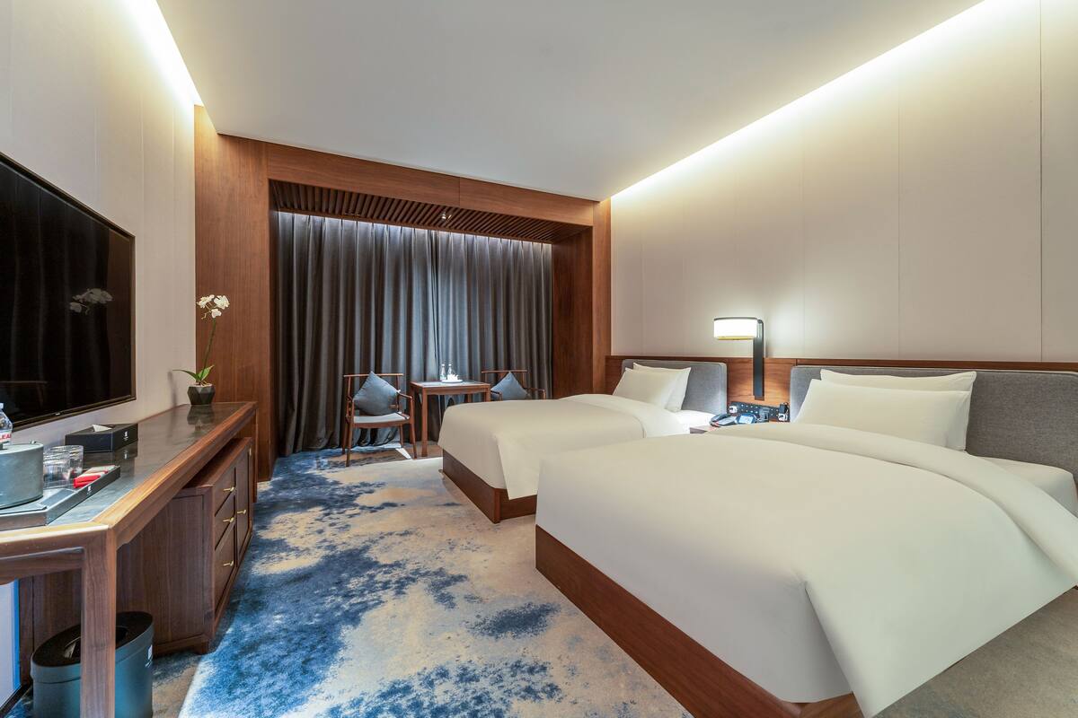A hotel room with two beds, a desk, a TV, and a small seating area.