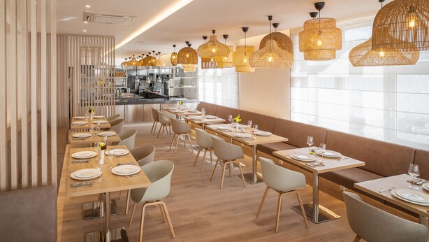 A modern restaurant with long wooden tables, cushioned benches, and woven pendant lights. - Hotel U Kaplicky (Pisek)