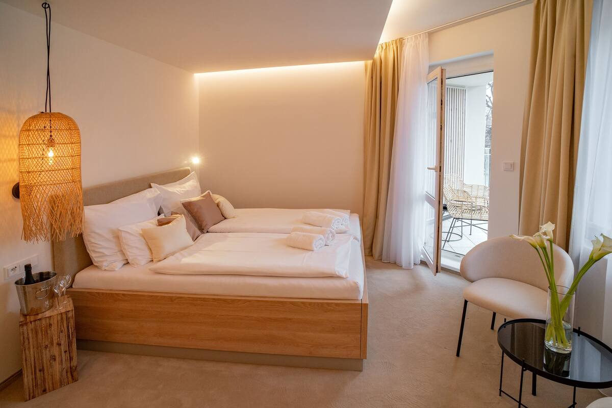 A modern hotel room with a large bed, a small table with a vase of flowers, and a chair.