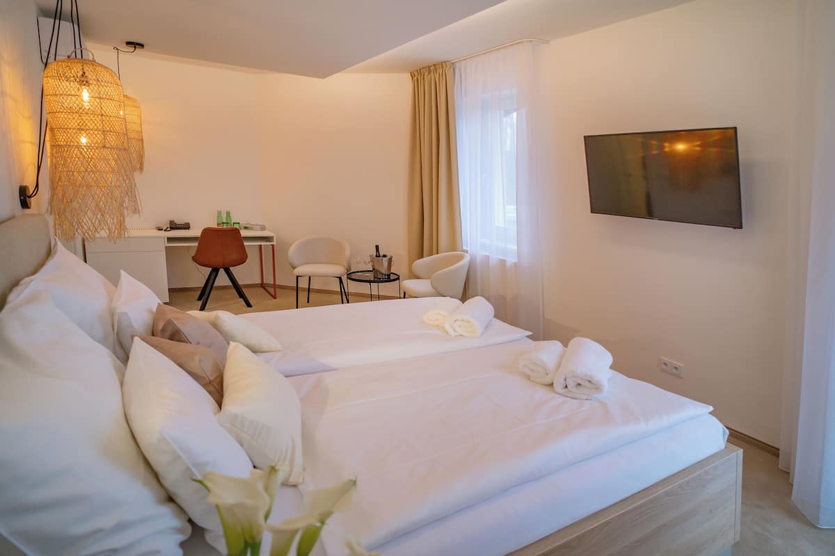 A hotel room with two beds, a desk, a chair, a TV, and a hanging light fixture.