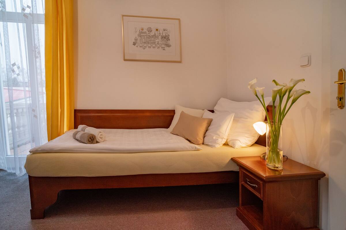 A neatly made bed with a wooden headboard, a bedside table with a vase of flowers, and a framed picture on the wall.