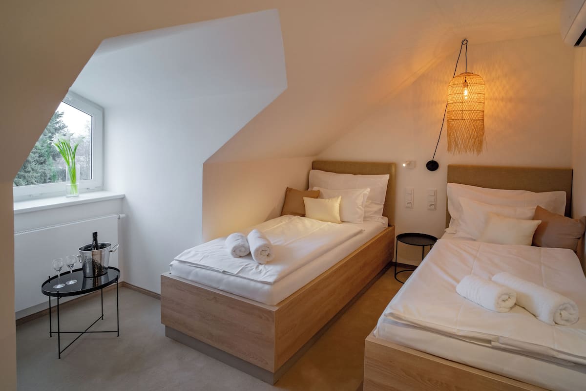 A bedroom with two beds, a small table with a bottle and glasses, and a hanging light fixture.