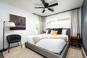 Um quarto moderno com uma cama grande, um ventilador de teto, um abajur e um quadro na parede.