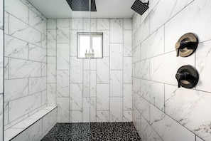 Een moderne badkamer met witte marmeren tegels, een zwart-wit betegelde vloer en een raam met flessen.