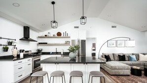 A modern kitchen with white cabinetry, a central island with bar stools, a grey sofa, and a black ceiling fan. - Swim up to cooking & entertainment, play corn hole, and relax by the fire at Cascada (Scottsdale)