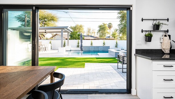 A modern kitchen with a large sliding glass door leading to a backyard with a pool, outdoor seating, and a pergola. - Swim up to cooking & entertainment, play corn hole, and relax by the fire at Cascada (Scottsdale)