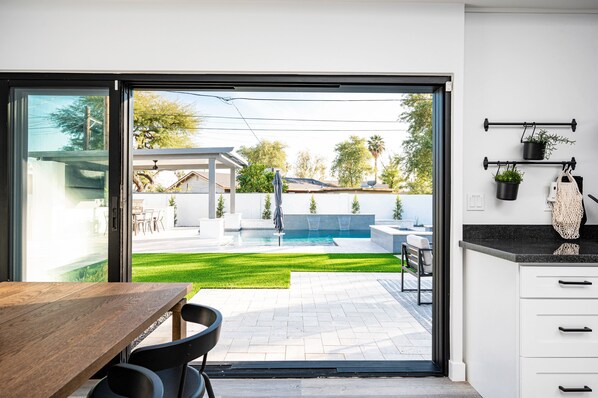 Cozinha moderna com uma grande porta de correr de vidro que dá para um quintal com piscina, área de estar ao ar livre e um pergolado.