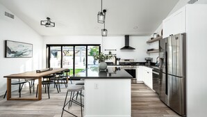 A modern kitchen with a large island, stainless steel appliances, and a dining area with a wooden table and chairs. - Swim up to cooking & entertainment, play corn hole, and relax by the fire at Cascada (Scottsdale)