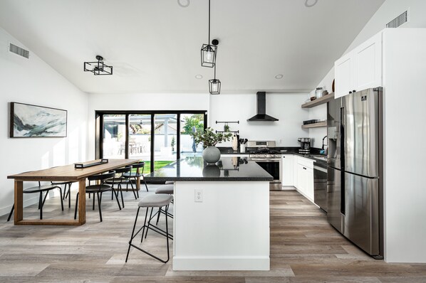 A modern kitchen with a large island, stainless steel appliances, and a dining area with a wooden table and chairs. - Swim up to cooking & entertainment, play corn hole, and relax by the fire at Cascada (Scottsdale)