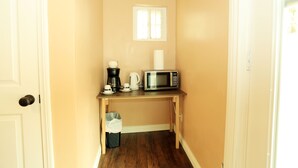 Un couloir étroit avec un bureau en bois, une machine à café, un four à micro-ondes et une poubelle.