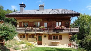 Une maison en bois à deux étages, dotée d’un balcon, d’un petit jardin et surplombant un ciel d’un bleu limpide.