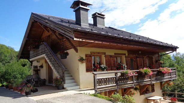 Un chalet traditionnel doté d’un balcon en bois, d’un escalier menant à l’entrée et de plantes en pot.