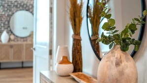 A modern bathroom with a wooden vanity, a round mirror, and a vase with green leaves.