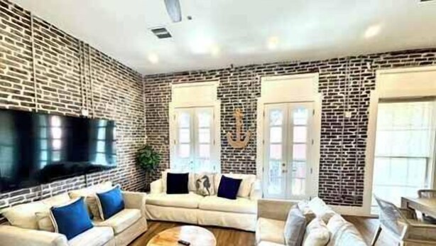 A living room with a brick wall, a flat-screen TV, two sofas, a coffee table, and a large window.