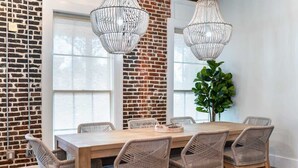 A dining area with a brick wall, large windows, wicker chairs, a wooden table, and hanging crystal chandeliers.