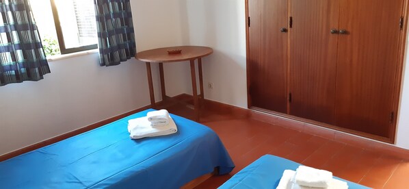 Ein Zimmer mit zwei Betten, einem kleinen runden Tisch und einem Holzschrank.