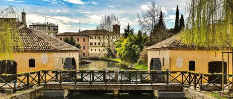 A canal with buildings on either side, a bridge with a railing, and a clear sky.