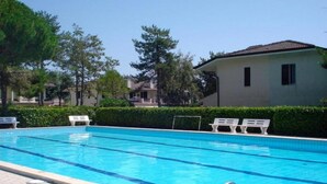 Une piscine à l’eau d’un bleu cristallin, entourée de chaises longues blanches et d’une haie.