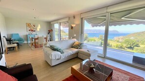 Un salon moderne avec un canapé blanc, une table basse en verre et une vue sur la mer.