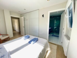Een slaapkamer met een bed, twee handdoeken, een stoel, een kledingkast en een badkamer zichtbaar door een geopende deur.