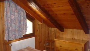 Une pièce de cabane en bois comprenant un lit, une commode et une fenêtre avec des rideaux.