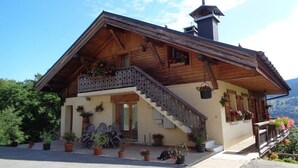 Un chalet en bois doté d’un balcon, de plantes en pot et d’un escalier menant à l’entrée.