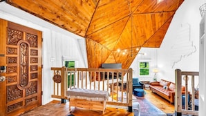 A cozy loft-style room with a sloped ceiling, wooden flooring, a wooden bench, a sofa, and a large window offering a view of greenery. - Unique Dome with HotTub & Mtn Views (Bryant Pond)