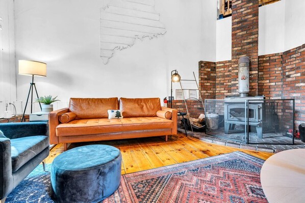 Ein gemütliches Wohnzimmer mit einer Ledersofa, einem blauen Hocker, einem gemusterten Teppich und einem Kamin aus Ziegelsteinen.