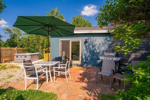 Ein Hinterhof mit einer Terrasse, einem Tisch, Stühlen, einem Grill und einem Whirlpool.