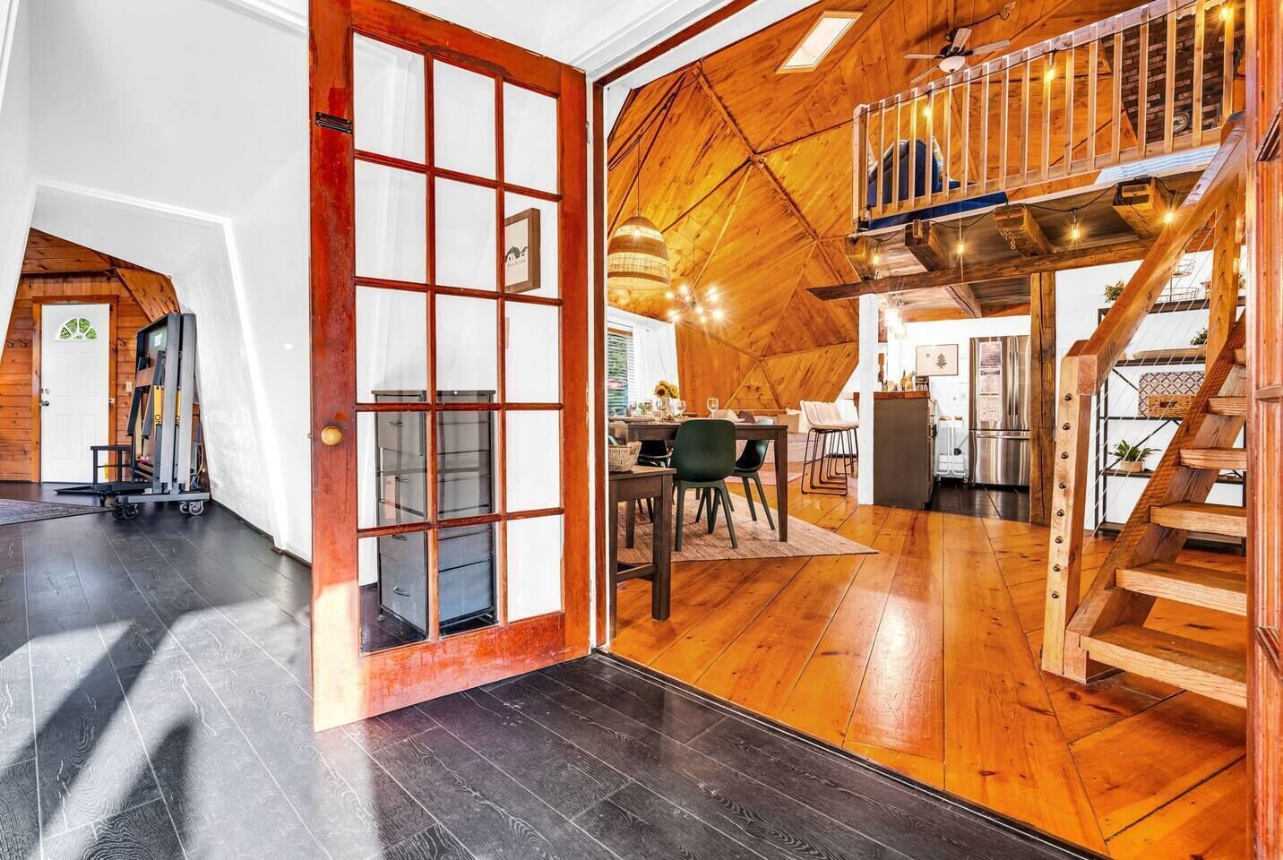 Een ruime kamer met een houten vloer, een eethoek met een tafel en stoelen, en een trap met een houten leuning.