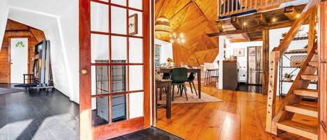 Een ruime kamer met een houten vloer, een eethoek met een tafel en stoelen, en een trap met een houten leuning.
