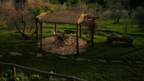 A rustic wooden gazebo with a stone floor and metal chairs, surrounded by lush greenery and a view of rolling hills in the distance. - Tuscan country house with enchanting view and swimming pool (Radicondoli)