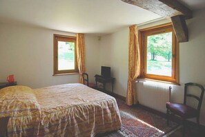 A bedroom with a bed, two windows, a radiator, a chair, and a television.