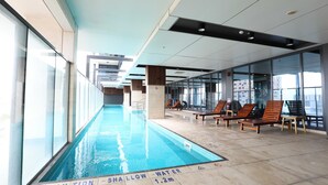 An indoor swimming pool with a shallow water warning, lounge chairs, and large windows. - 1 Bedroom Adelaide CBD Centre Apartment (Adelaide)