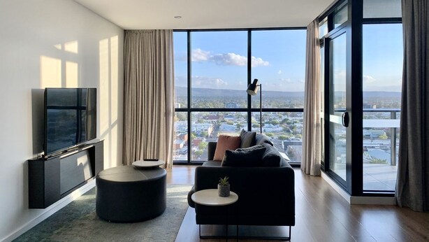 A modern living room with a large window, a flat-screen TV, a sofa, and a small side table. - 1 Bedroom Adelaide CBD Centre Apartment (Adelaide)